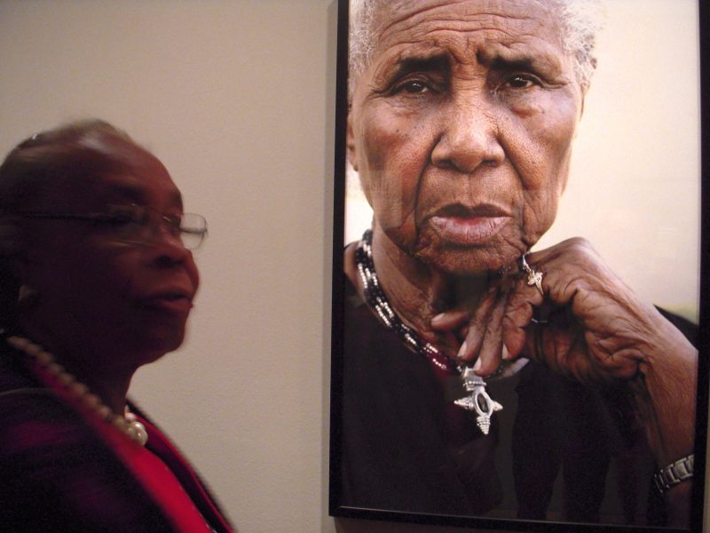 Mary Lee Bendolph in front of Linda Day Clark photo of one of the quilters.
