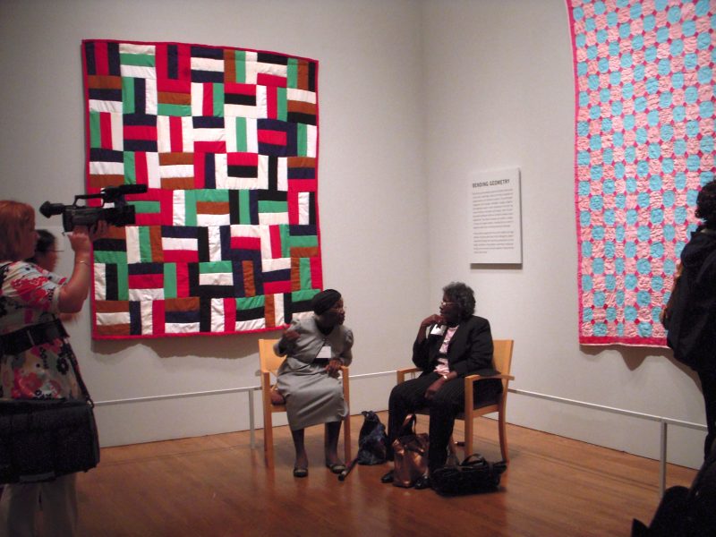 Two Gees Bend quilters sit in front of their quilts at the PMA's press preview.