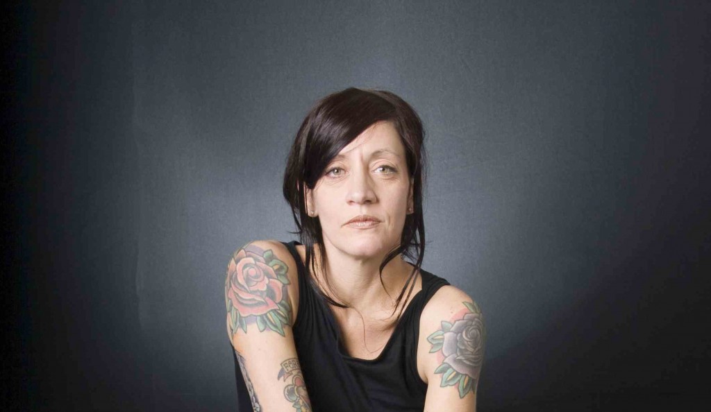 photo of woman looking concerned, dark hair, dark t-shirt, tattooed arms