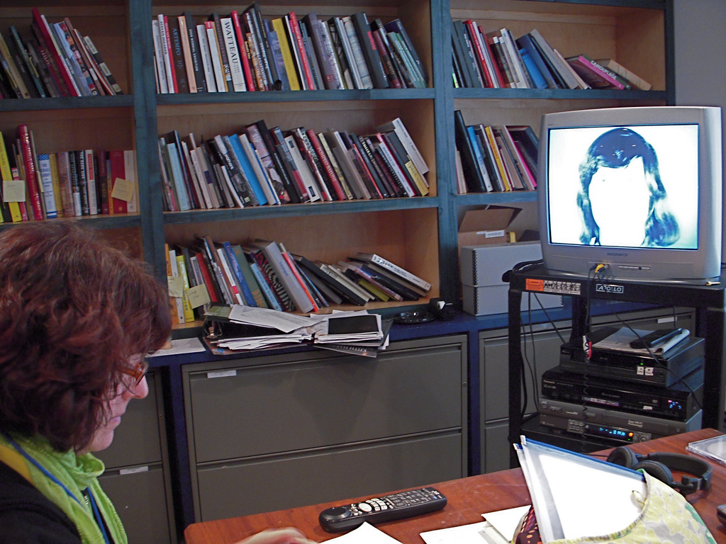 Library with woman looking at tv screen with woman's image on screen.