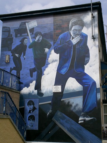 The Runner: Derry, Northern Ireland. This mural was erected to warn young people of the dangers of becoming involved with the conflict. The mural depicts young boys coughing and running from a canister of CS gas that has just been fired. Scenes like this were frequent during the height of the Troubles. In the bottom left hand corner of this mural are two portraits of young boys. The top boy is Manus Derry who was killed when he was just 15 years old. Manus was killed on May 19 1972 when he was hit by fragments from a ricochet bullet fired by a British Army sniper from an observation post on the city walls.