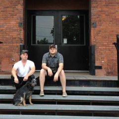 Ryan McCartney, Henry the dog, and Tim Belknap sitting in front of the Crane Arts Building.