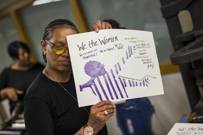 Faith Bartley holding a poster made in this year's Women in Re-Entry Project of the People's Paper Co-Op