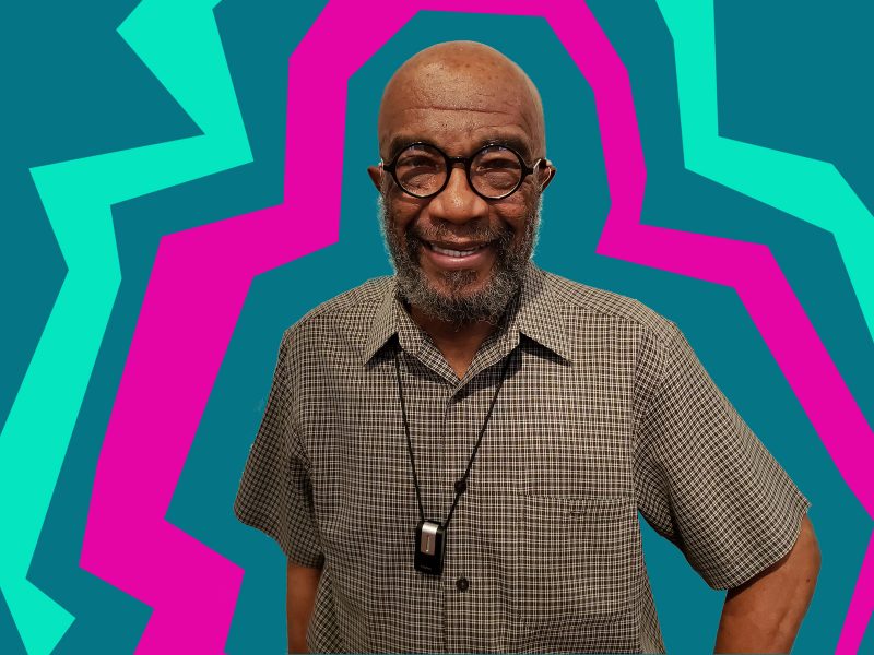 A Black man wearing a short sleeve shirt and glasses looks at you. Bold, graphic lines of pink and green radiate around him.
