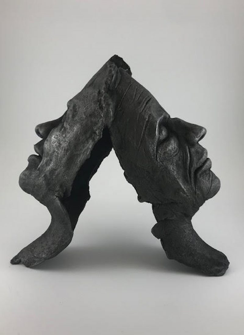 Sculpture of the profile of two faces without the back of their heads, each leaning backwards onto each other.