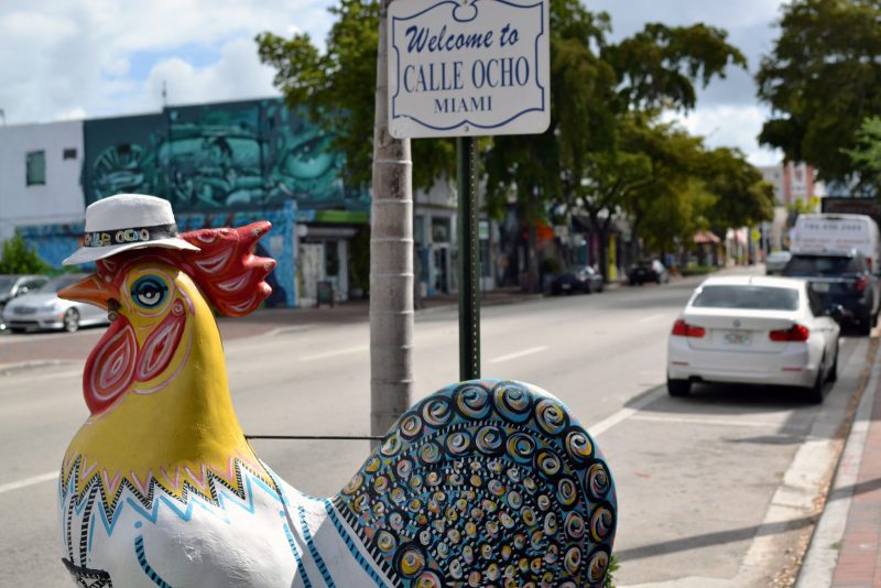 Sculpture of a rooster with decorative painting in front of a sign that says "Welcome to Calle Ocho Miami"