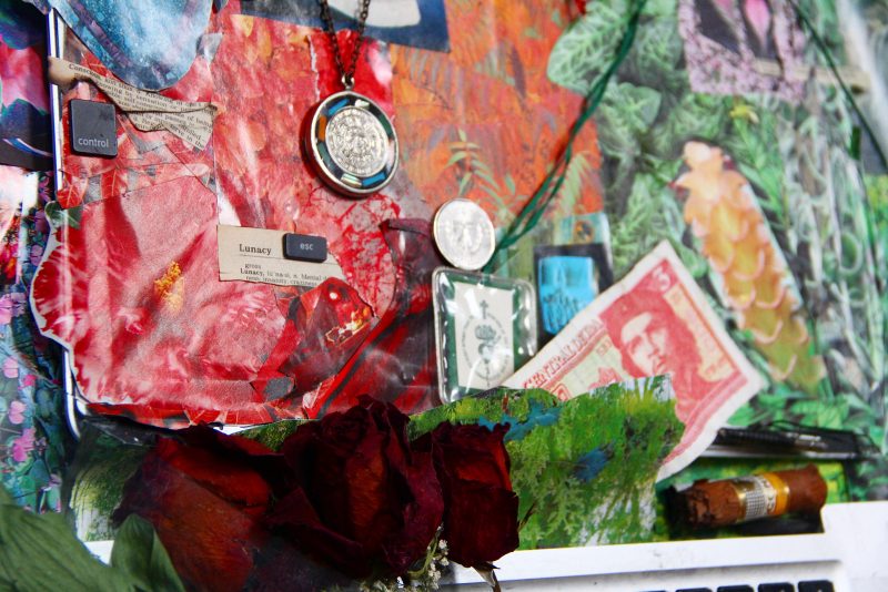 Close up of a collage containing technology, flowers, broken cell phone, cuban currency, roses, necklaces, and more, framed.