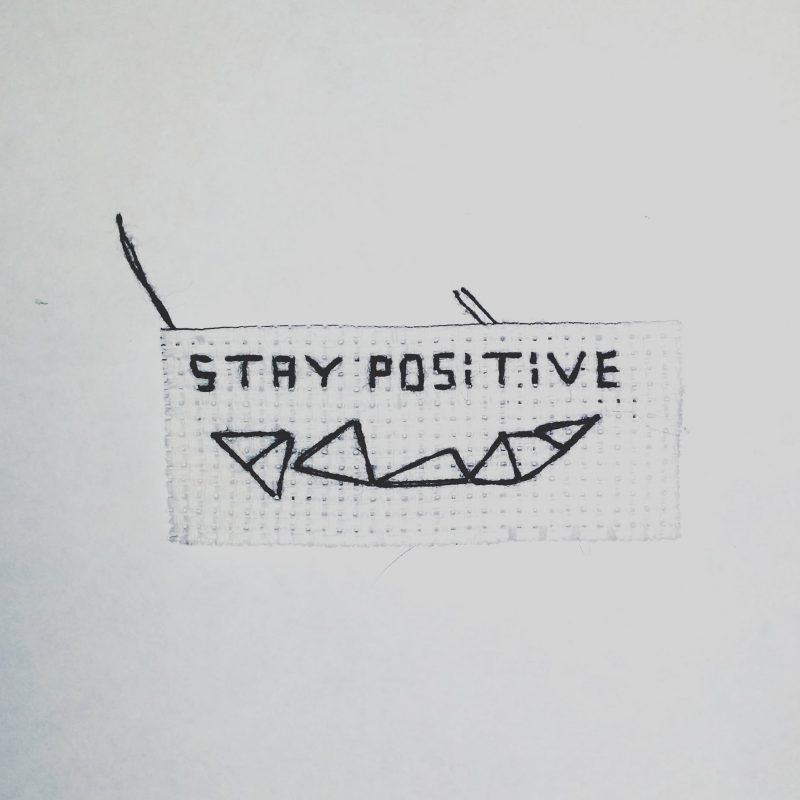 Small white rectangle with "stay positive" and a pattern made out of triangles stitched onto it.