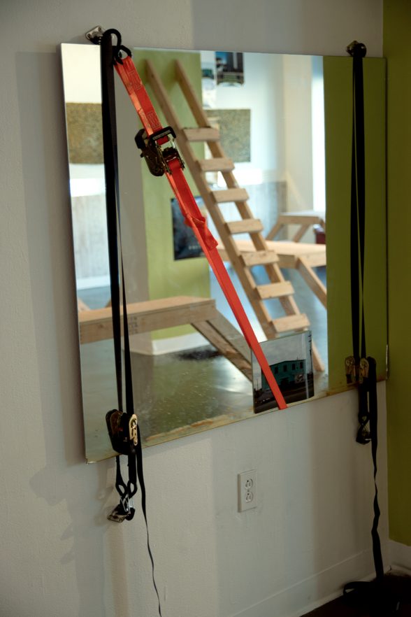 Mirror with ratchet straps on them. In the reflection is a wooden ladder and a wooden bench.