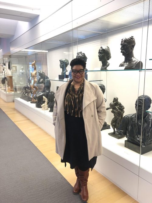 Photo of Brittany Webb, curator of the John Rhoden Collection at Pennsylvania Academy of Fine Arts, in front of a glass case of portrait sculptures (busts).