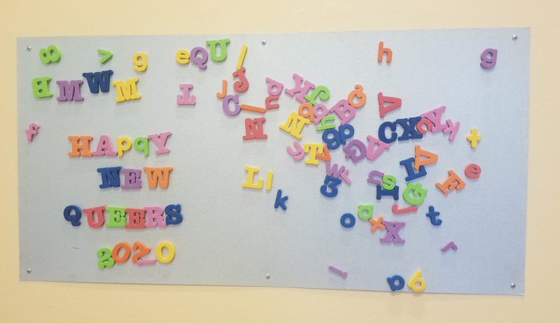 Magnetic board with colorful letters, on the left spelling "Happy New Queers 2020"