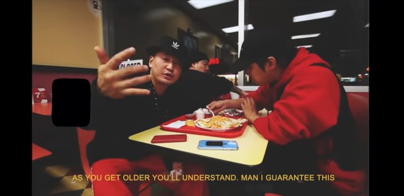 Three people eating food at a restaurant dressed in a red and black and gesturing with a text overlay that says "As you get older you'll understand. Man I guarantee this"