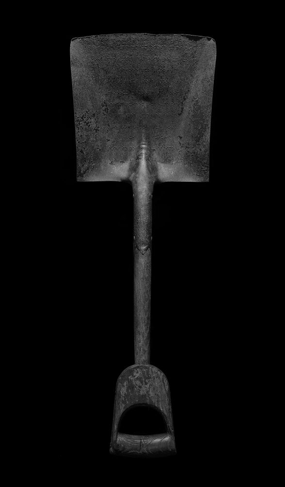 Above view of gray shovel on black background, handle facing south