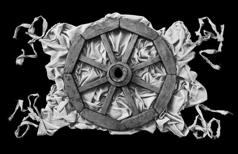 Above view of black and white wooden wheel on light gray rumpled cloth on a black background