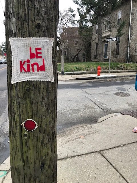 Fabric stitched with "be kind" hung on a telephone pole