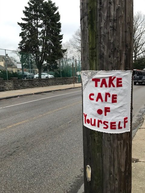 Fabric stitched with "take care of yourself" hung on a telephone pole