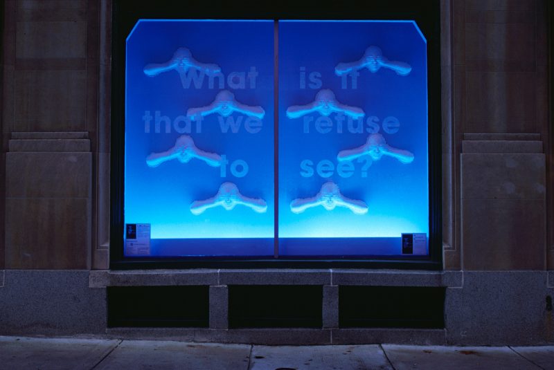 Blue window display of heads with hands over their eyes and the text: "What is it that we refuse to see?"
