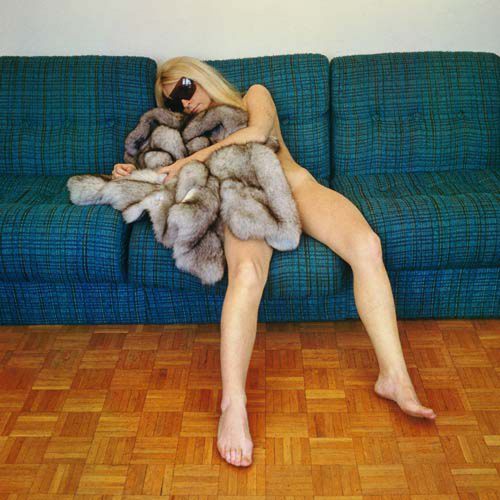 Natalia laying naked on a couch with sunglasses and a fur covering her body.