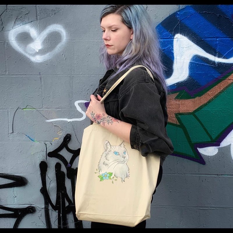 Woman modeling Mandi Spicer's tote bag with a drawing of a cat on it.