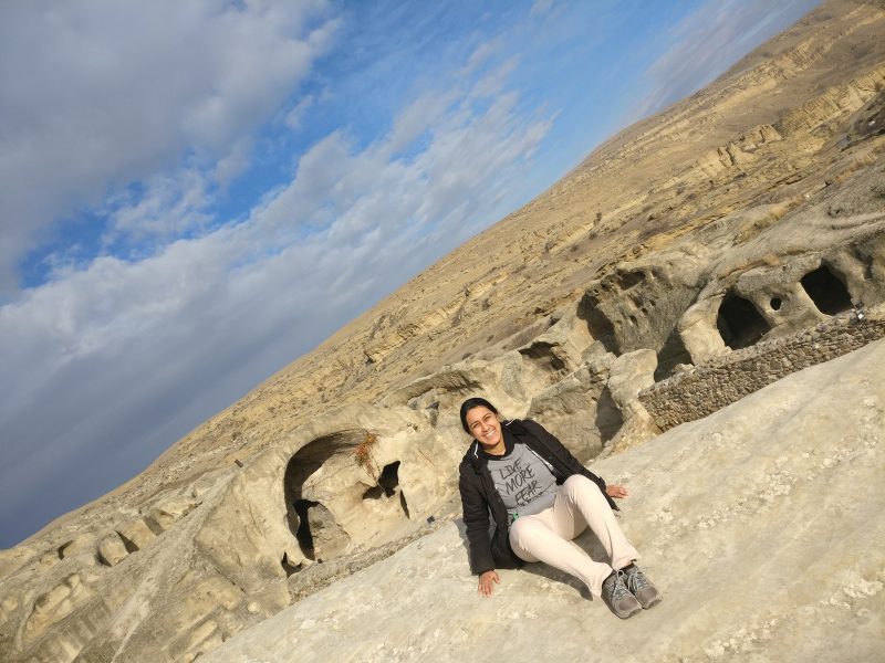Krishna Desai sitting on a giant rock in front of caves.