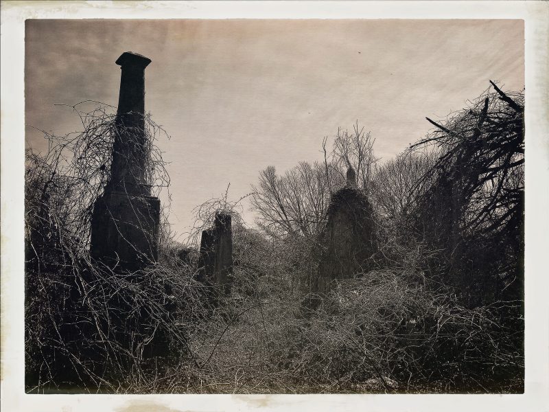 Black & white photo of a graveyard with three tall gravestones.