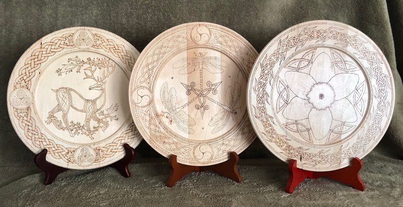 Wooden plates with ornate designs burned into them on wooden stands.