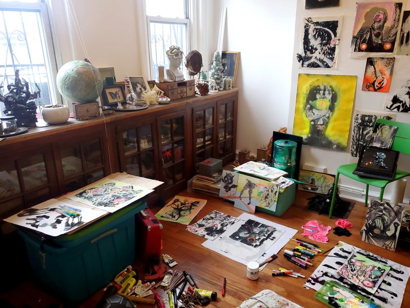 Artist's home studio with paintings on wall, floor, tables