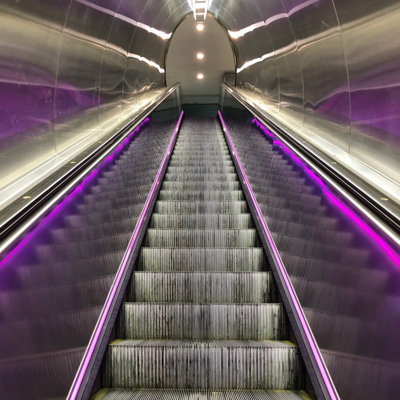A long escalator with purple lighting running up the sides.