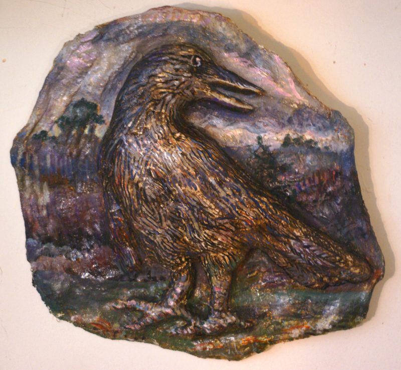 A sculpture of a crow coming out of a circular painted wooden surface.