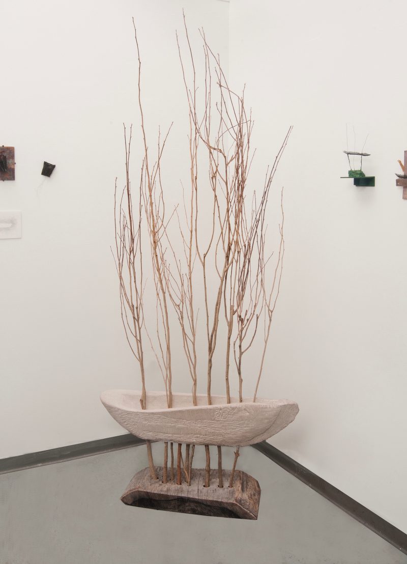 Wooden sculpture of a boat with branches growing up through it and elevating it.