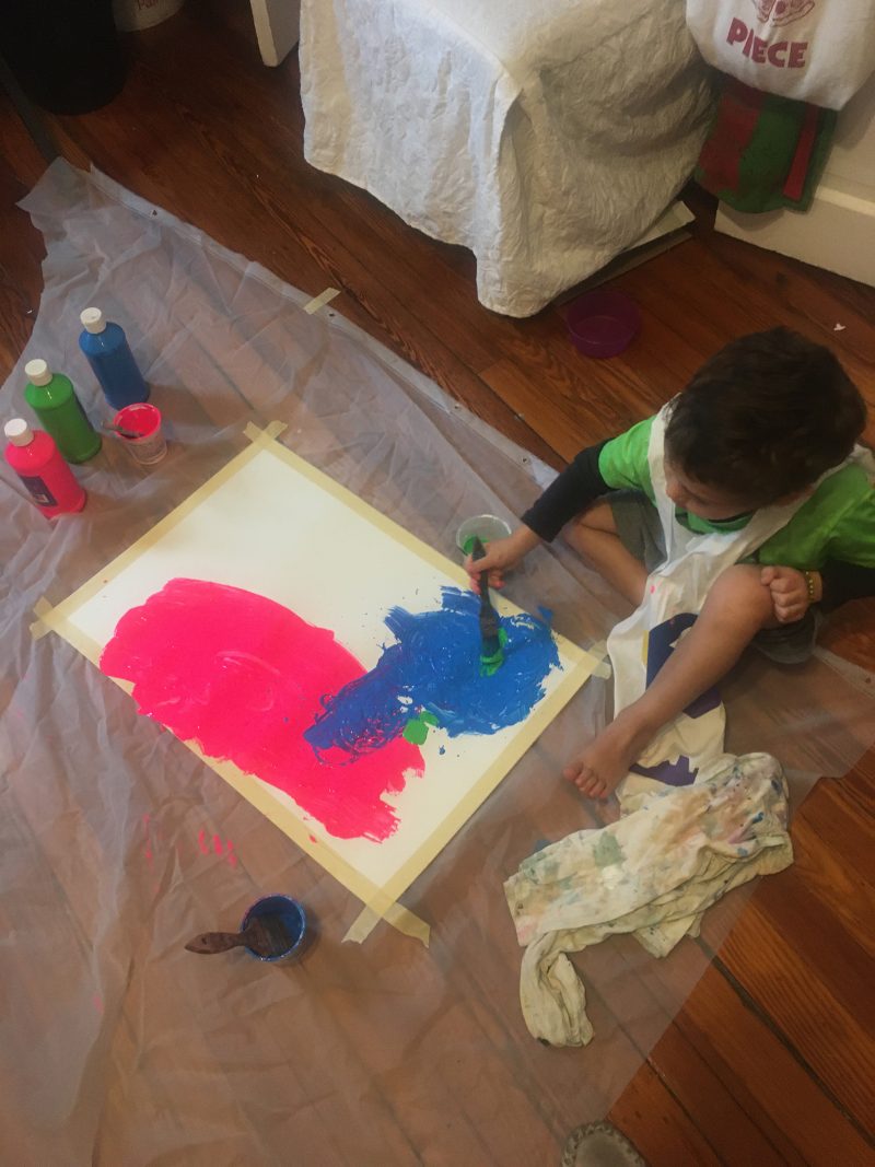 Young child sitting on the floor painting with bright colors.