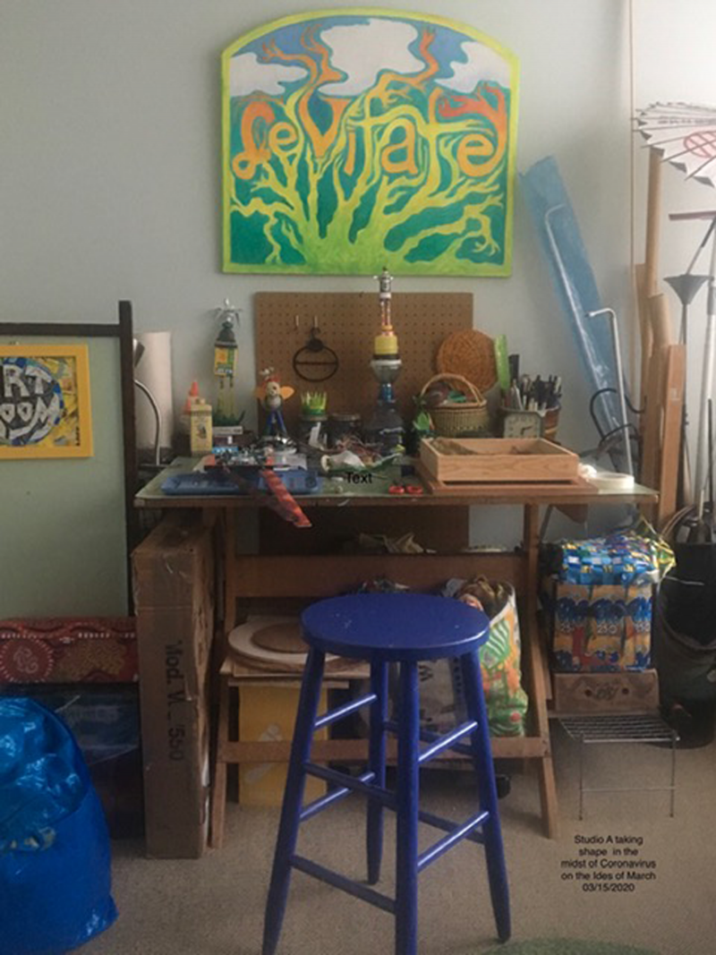 Desk with art supplies and a painting that says "Leviate" hanging above it.