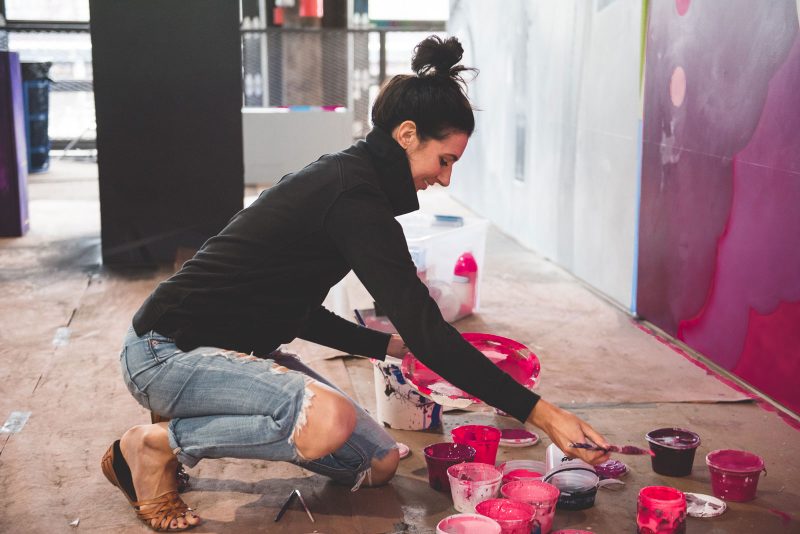 Ali Williams hunched over buckets of paint, loading her brush with paint.