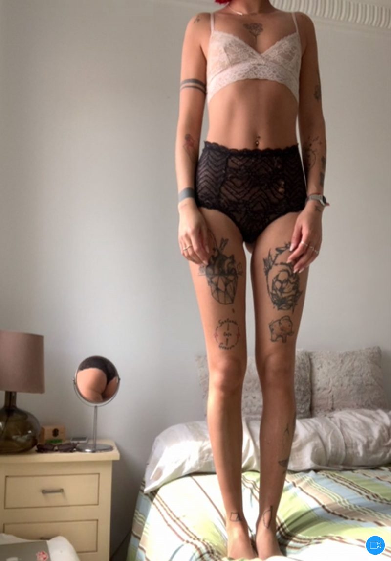 Front view of the neck down of a woman standing on her bed in underwear.