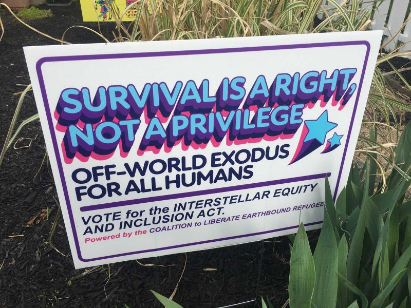 Lawn sign that says "SURVIVAL IS A RIGHT, NOT A PRIVILEGE / OFF-WORLD EXODUS FOR ALL HUMANS / VOTE for the INTERSTELLAR EQUITY AND INCLUSION ACT"