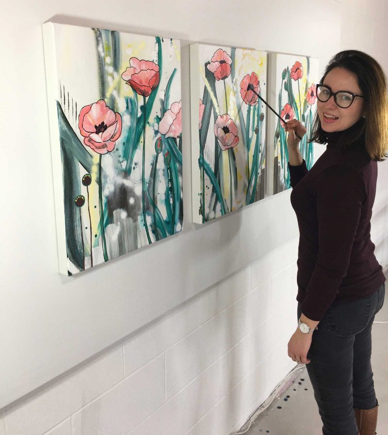 Mandy martin standing in front of her tryptych painting a stroke onto one of the three floral paintings.