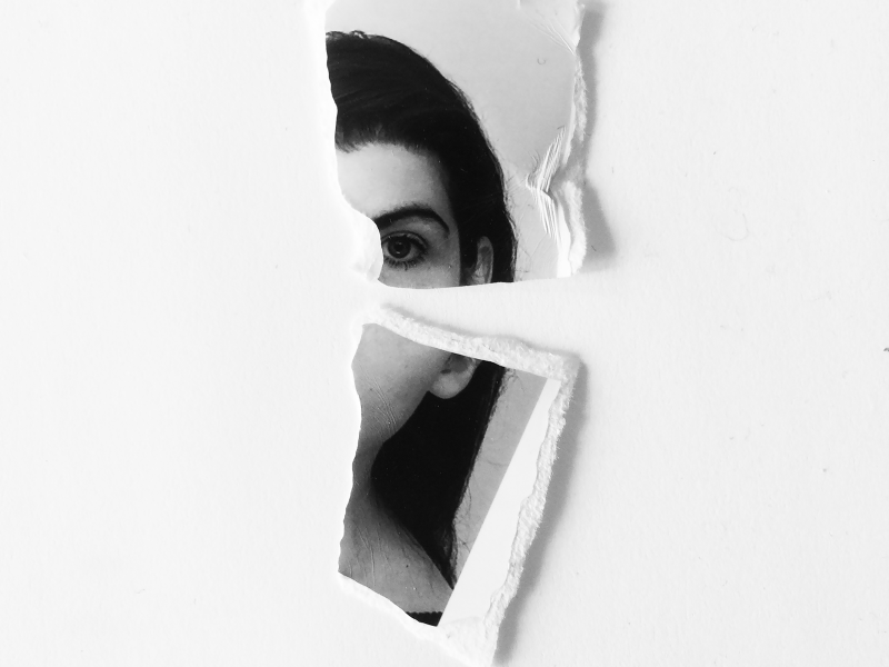 A torn photograph of a woman, visible is only their eye and left side of their face.