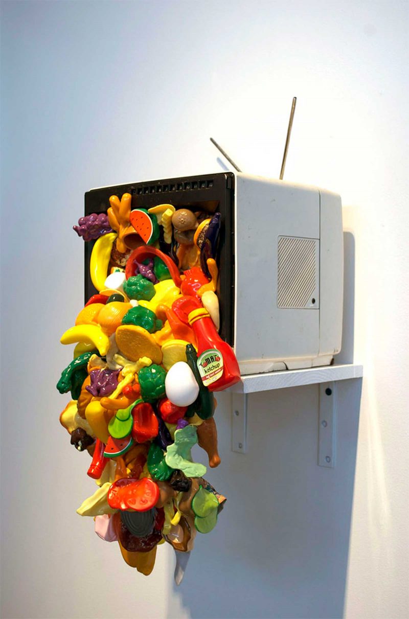 Sculpture of plastic toys flowing out of an old fashion TV with the screen missing.