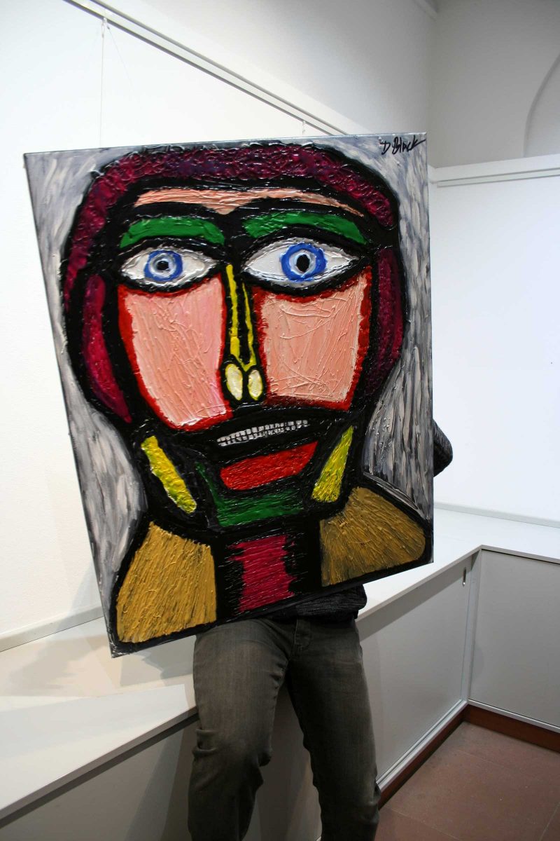 Darrell holding a painting of an abstracted portrait from the shoulders up