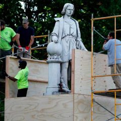 Columbus statue being covered by wooden boards by workers.