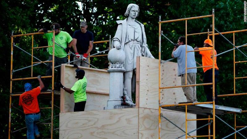 Columbus statue being covered by wooden boards by workers.