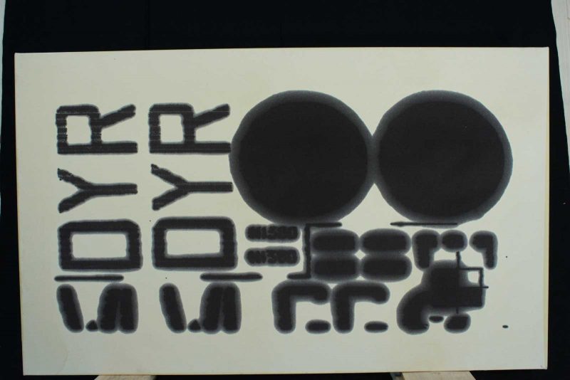 Black ink on white paper spelling out DYR two times sideways, with two large black circles to the right of it, and some black patterns underneath