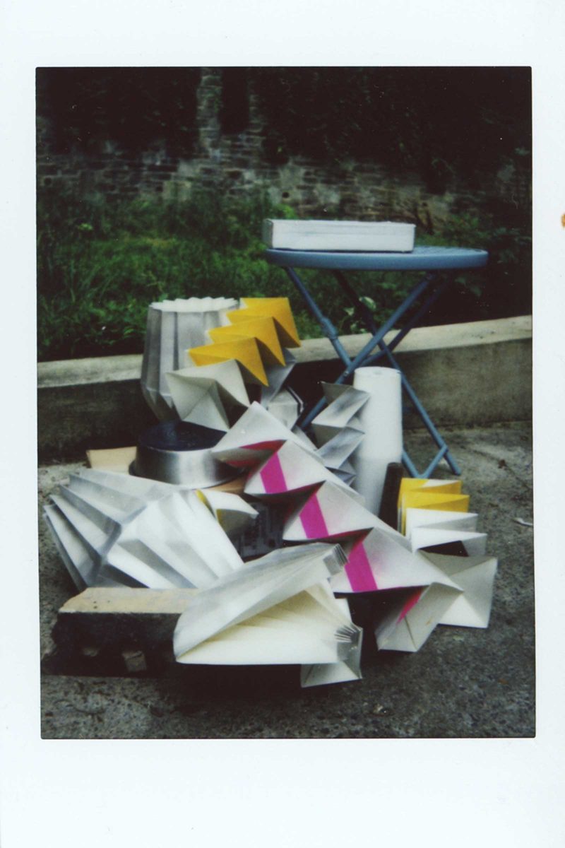 Photograph of a triangular sculpture leading up to a blue table with a box on it in a outdoor space
