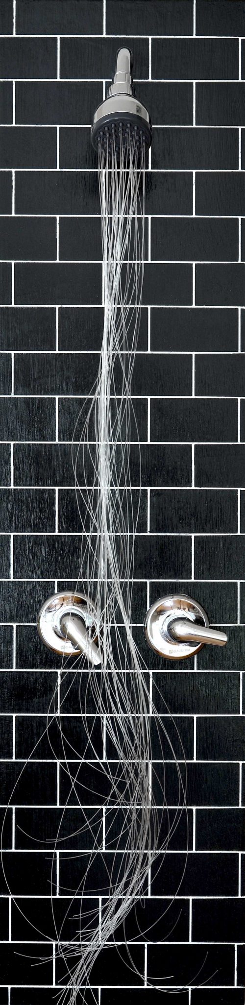 Long vertical image of a shower head with silver colored hair-like material hanging out of it