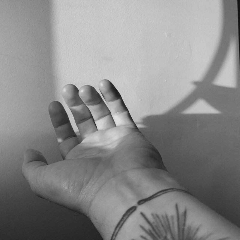 Black & white photo of Juno's left hand with a tattoo of lines extending from a central point.
