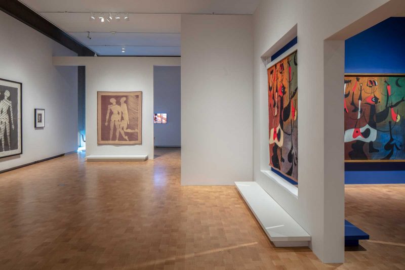 Gallery view with large pieces visible in a white room with a blue room next to it. 