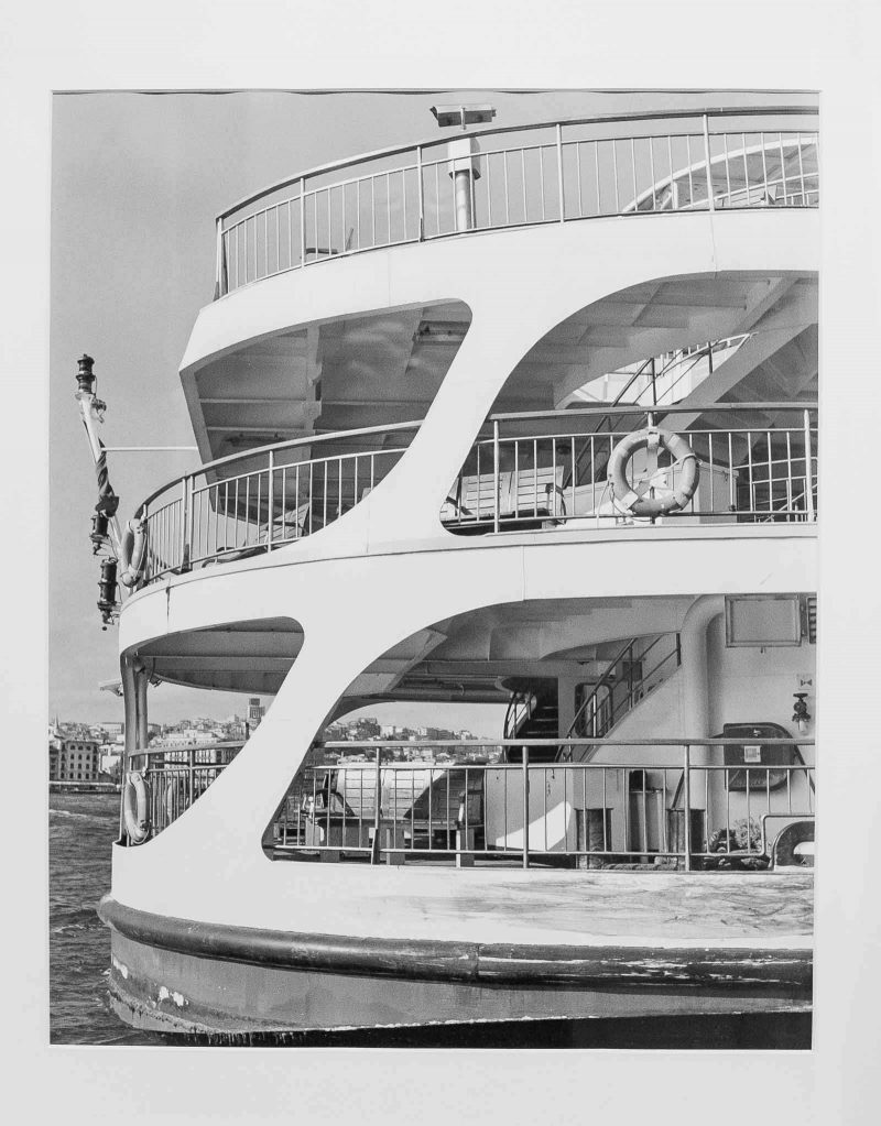 Black & White photograph of a super yacht seen from the side so that a lower deck, middle deck, and sun deck are visible.