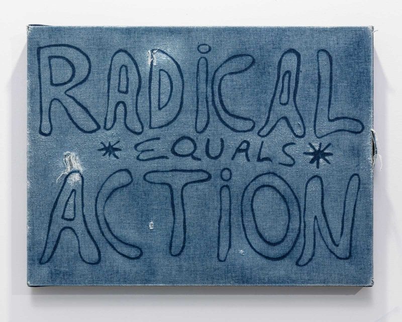 "Radical Equals Action" written on denim stretched onto a wooden rectangle like a painting