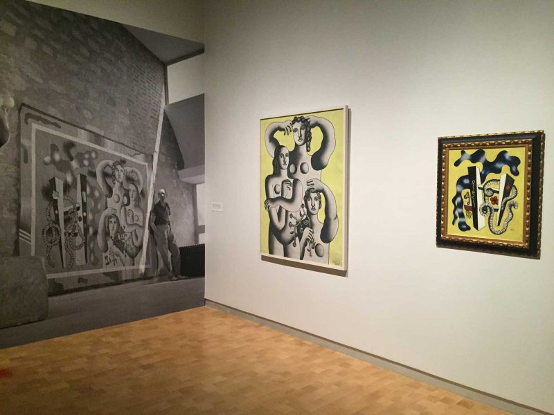 View of the exhibition with a black and white print of pieces on the wall with the same piece framed and shown on the adjacent wall. 