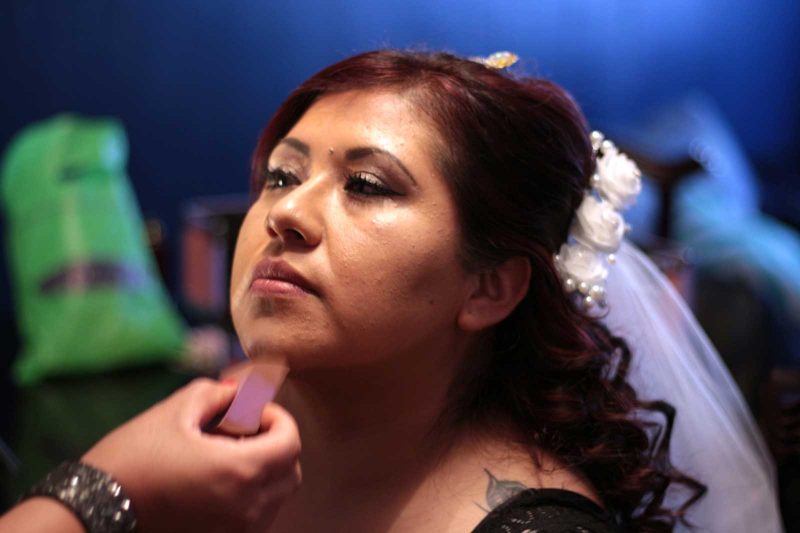 Close-up view of someone applying makeup on another person who has their hair half up and half down with flowers pinned in.